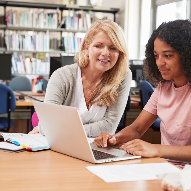 Autistic Teenager at School sitting next to her teacher.