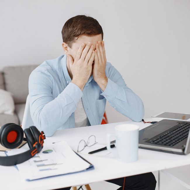 Time Blindness can affect autistic and adhd individuals. This photo is of a young man at his desk with his hands over his eyes and his head down