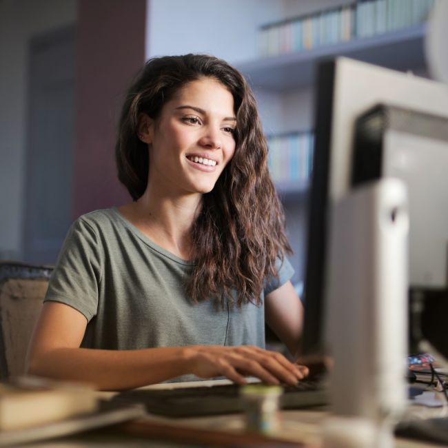 A young lady with dark long hair sitting at a desk with a computer reading Gaming-and-Life-Skills-Development